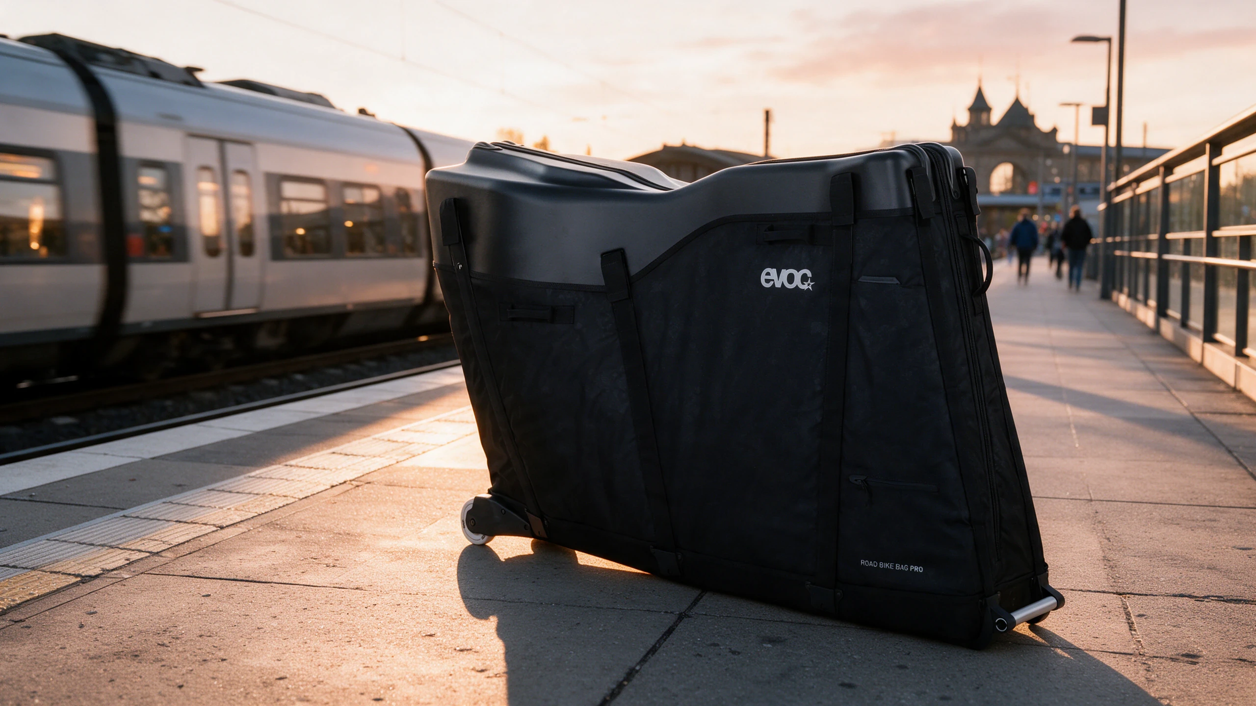 Gepackter EVOC Road Bike Bag Pro auf einem Bahnsteig im Abendlicht, daneben ein Zug